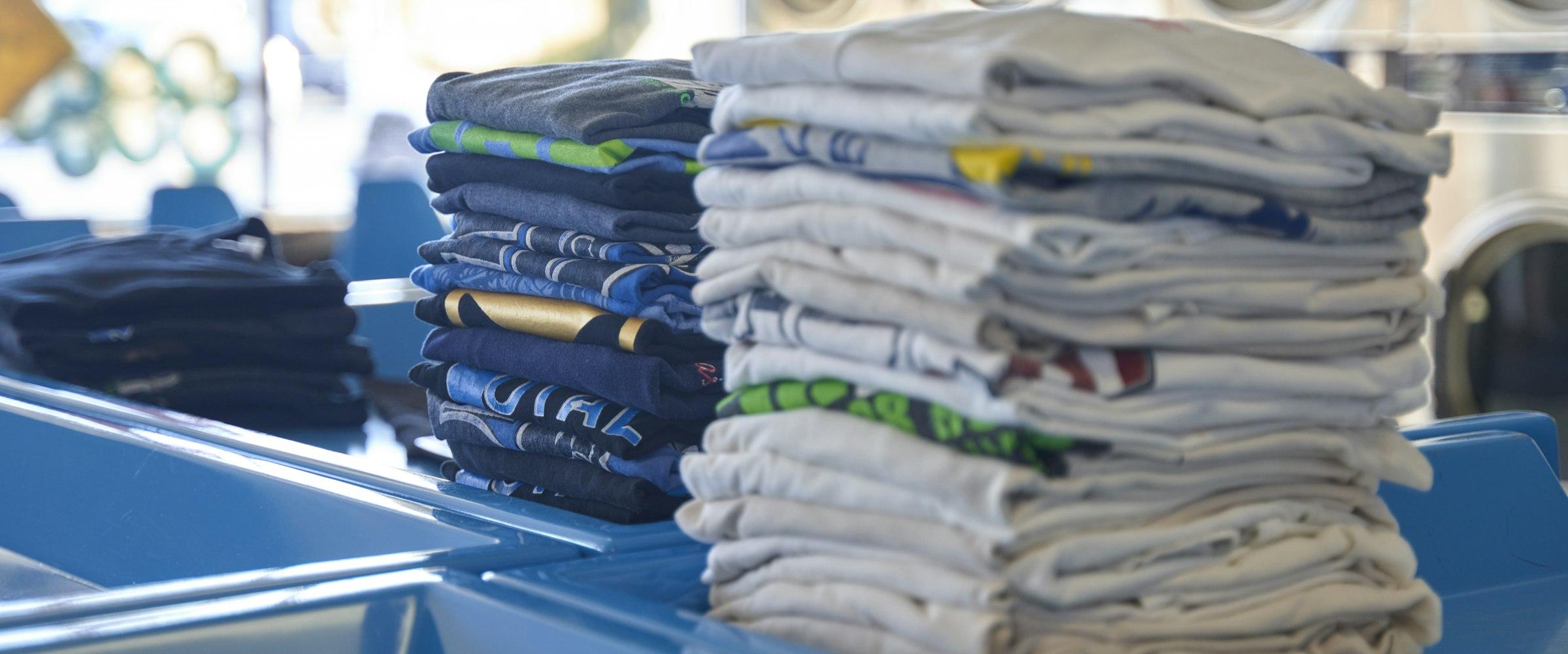 Stacks of neatly folded clean laundry, with washing machines in the background