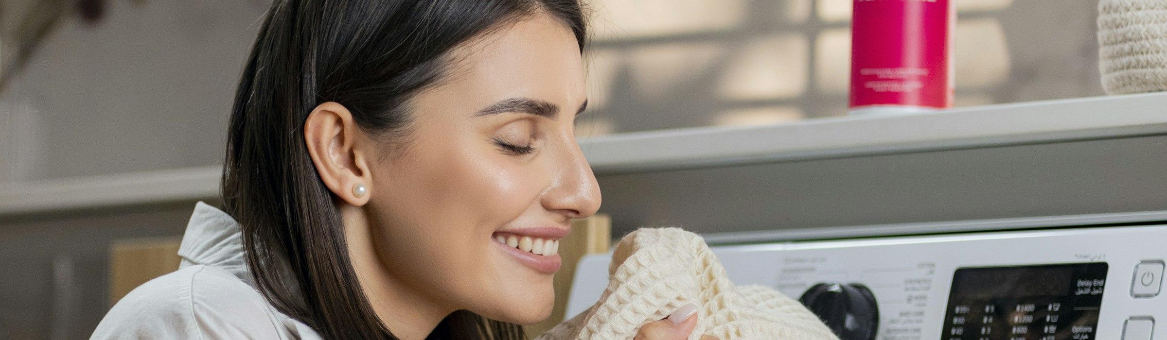 A smiling woman holding a fresh, clean towel up to her face